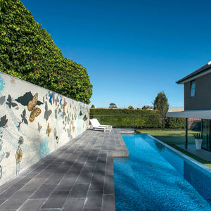 Butterfly mosaic mural on outdoor wall, swimming pool with glass tile, and porcelain patio pavers