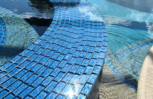 Blue mosaic tiles on a pool edge with water reflection