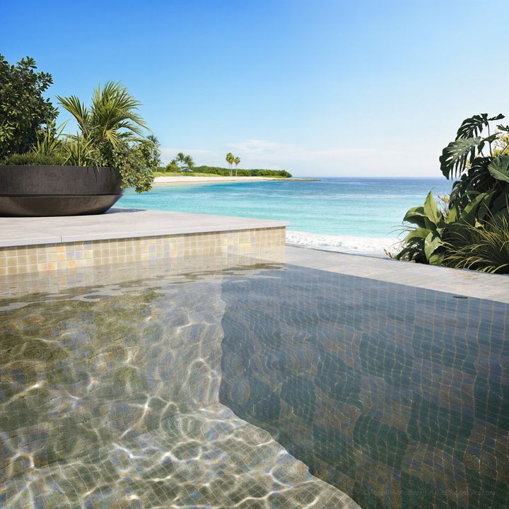 Pool area with clear water, tiled floor, and tropical plants overlooking a beach.