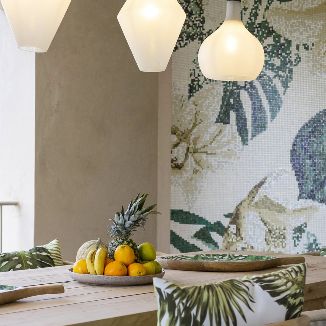Dining area with a table, fruit bowl, and decorative pillows against a floral mosaic wall.