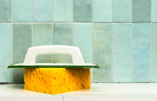 Yellow sponge with a white handle on a tiled bathroom wall background