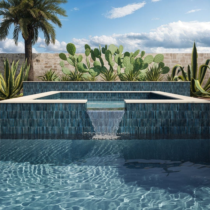 Modern pool with blue tiles surrounded by cacti and a palm tree under a clear sky.