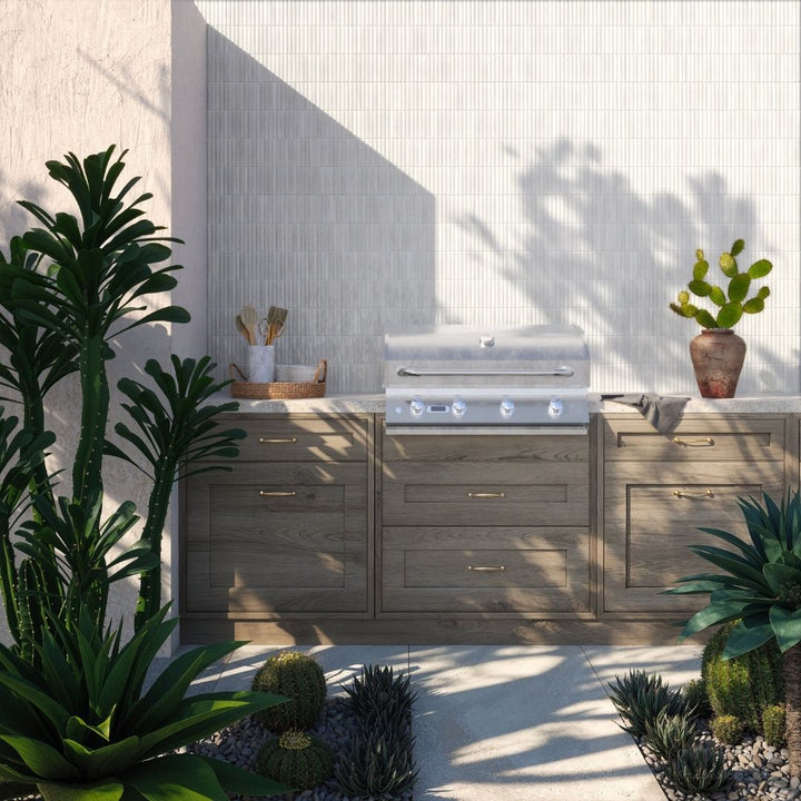Outdoor kitchen with wooden cabinets and a grill, surrounded by plants.