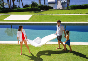 Family carrying a modern white in-pool chaise lounger beside a swimming pool