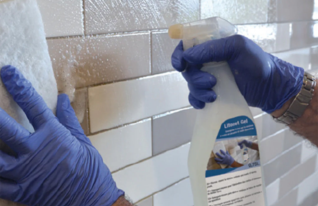 Person wearing blue gloves cleaning a tiled wall with a spray bottle labeled 'Limeine Gel'.