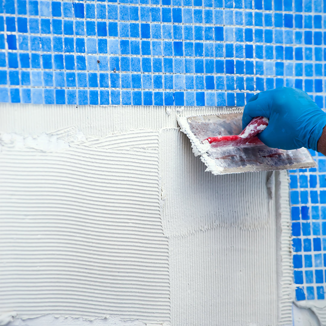 Person applying white material to a pool edge with blue mosaic tiles in the background