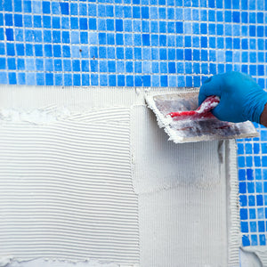 Person applying white material to a pool edge with blue mosaic tiles in the background