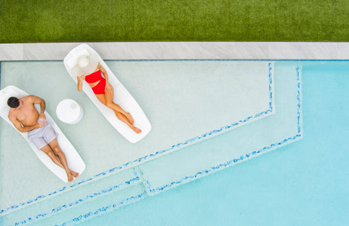 Two people on in pool loungers on swimming pool baja shelf